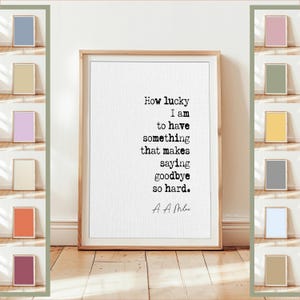 May include: A framed print with the quote "How lucky I am to have something that makes saying goodbye so hard." The text is in black on a white background, within a light brown wooden frame. The image is displayed on a wooden floor.