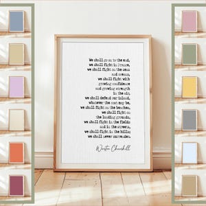 Könnte beinhalten: Ein gerahmter Druck mit einem Holzrahmen zeigt ein Zitat von Winston Churchill. Das Zitat ist in schwarzem Text auf weißem Hintergrund. Der Druck wird auf einem Holzboden mit einer weißen Wand angezeigt. Verschiedene kleine, farbige quadratische Drucke sind um den Hauptdruck angeordnet.