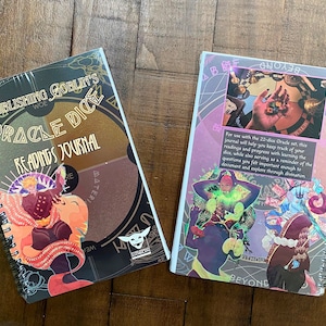 May include: Two spiral bound journals with colorful covers. The journal on the left has a gold and black cover with the text "The Publishing Goblin's Woe Oracle Dice Readings Journal". The journal on the right has a purple and pink cover with a collage of images and the text "For use with the 22-die Oracle set, this journal will help you keep track of your readings and progress with learning the dice, while also serving as a reminder of the questions you felt important enough to document and explore through divination."