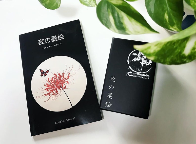Puede incluir: Dos libros negros con texto blanco en las portadas. El libro de la izquierda tiene una flor roja y una mariposa en la portada. El texto en la portada dice "Yoru no Sumi-e" y "夜の墨絵". El texto en el libro de la derecha dice "夜の墨絵".