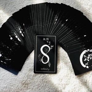 Puede incluir: Una baraja de cartas de tarot negras con tinta blanca, que presenta un s&iacute;mbolo de infinito y la palabra "Infinity" en la carta de la parte delantera. Las cartas est&aacute;n desplegadas en semic&iacute;rculo.