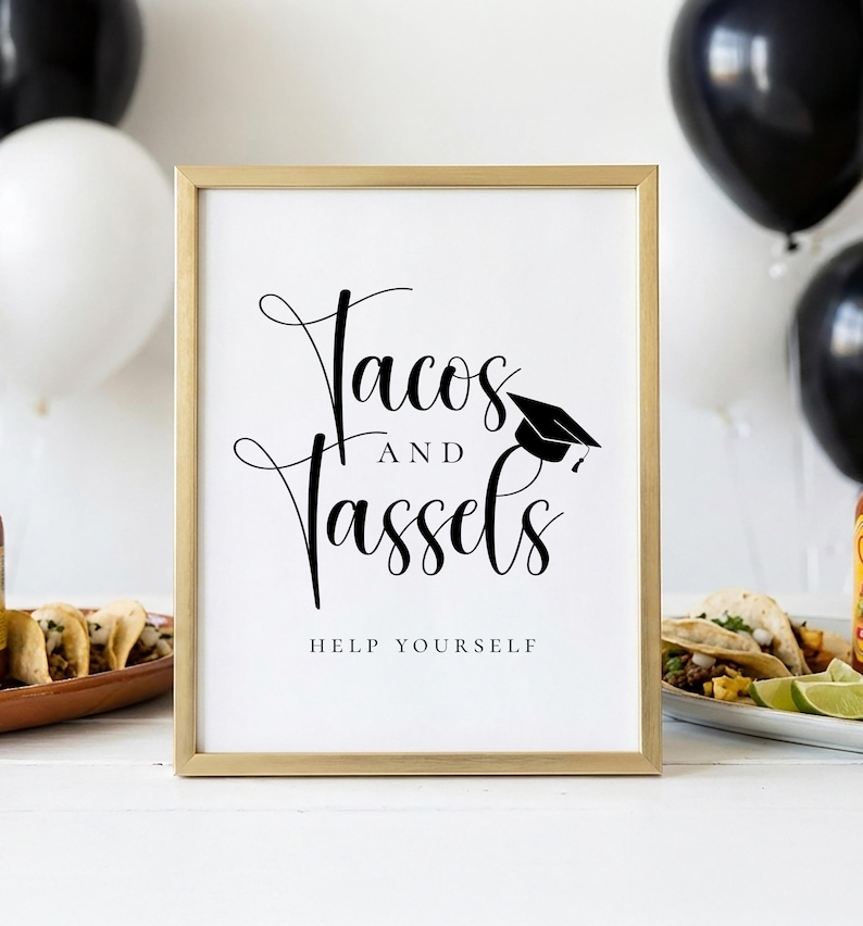 Op de afbeelding: Een ingelijst bord met de woorden "Tacos and Tassels" in elegant schrift, vergezeld van een afstudeerpet-afbeelding. De zin "Help Yourself" staat eronder gedrukt. Het bord staat in een gouden lijst, met zwarte en witte ballonnen op de achtergrond.