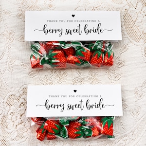 May include: Two clear cellophane bags filled with strawberry-shaped candies. Each bag has a white label with the text "THANK YOU FOR CELEBRATING A berry sweet bride" in black script, topped with a black heart.
