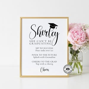 Può includere: Un cartello incorniciato con bordo dorato, a tema laurea. Il cartello presenta il nome "Shirley" in elegante corsivo, insieme a ricette di bevande. Un mazzo di fiori rosa in un barattolo di vetro è accanto.