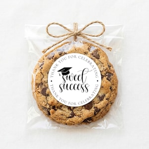 Op de afbeelding: Een chocolate chip cookie in een doorzichtige cellofaan zak, vastgebonden met touw. Een ronde sticker op de cookie leest "Sweet Success" met een afstudeerhoedje en de woorden "Thank you for celebrating."