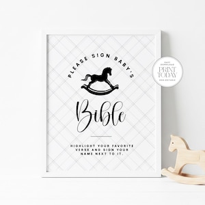 May include: A framed print with the text "PLEASE SIGN BABY'S Bible" and a rocking horse illustration. The print includes instructions to highlight a favorite verse and sign a name. The background has a subtle plaid pattern.