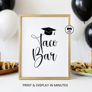 Op de afbeelding: Een ingelijst bord met de woorden "Taco Bar" in elegant zwart schrift, bekroond met een illustratie van een afstudeerpet. Het bord staat in een gouden lijst, met de tekst "PRINT & DISPLAY IN MINUTES" onderaan. Ballonnen zijn op de achtergrond.