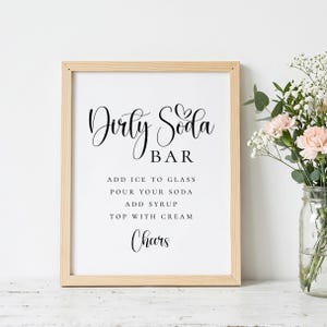 Puede incluir: Un cartel enmarcado con las palabras "Dirty Soda Bar" en escritura elegante. Debajo, las instrucciones dicen "A&ntilde;adir hielo al vaso, verter tu refresco, a&ntilde;adir jarabe, cubrir con crema, &iexcl;Salud!". El marco es de madera clara.