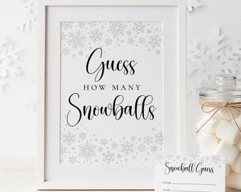 May include: A framed sign with the text "Guess How Many Snowballs" in elegant script, surrounded by snowflake designs. A small card with "Snowball Guess" text and a jar of marshmallows are also present.