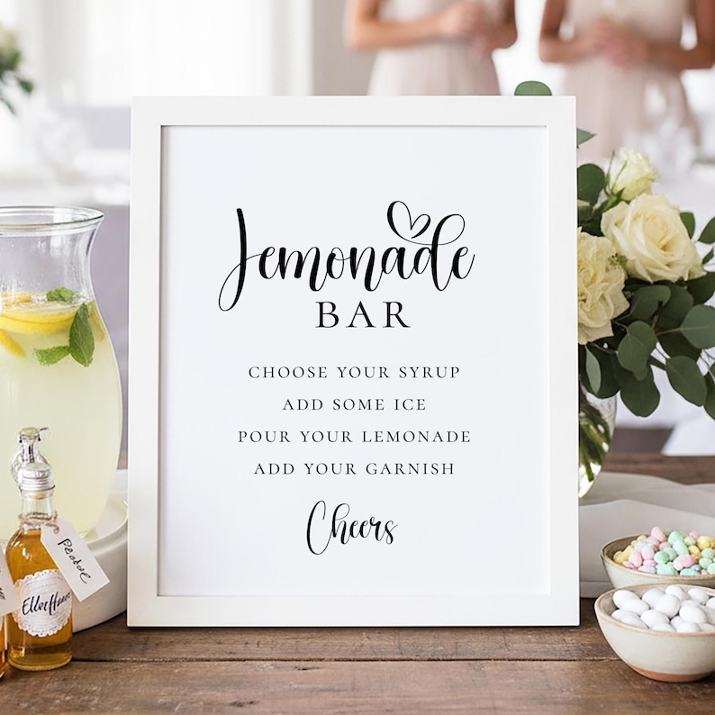 Puede incluir: Un letrero enmarcado en blanco con las palabras "Lemonade Bar" en escritura elegante. Debajo, las instrucciones dicen "Elige tu jarabe, a&ntilde;ade hielo, vierte tu limonada, a&ntilde;ade tu guarnici&oacute;n, &iexcl;Salud!" Se ve una jarra de limonada y botellas peque&ntilde;as.