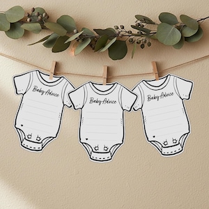Op de afbeelding: Drie witte kaarten in de vorm van een babyromper met de tekst "Baby Advice" zijn met houten knijpers aan een touwtje bevestigd. De kaarten hebben een gelijnd gedeelte om op te schrijven en zijn versierd met een zwarte omtrek. Eucalyptustakken erboven.
