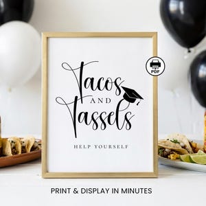 May include: A framed sign with the words "Tacos and Tassels" in elegant script, featuring a graduation cap graphic. The phrase "Help Yourself" is below the main text. The sign is in a gold frame, with balloons in the background.