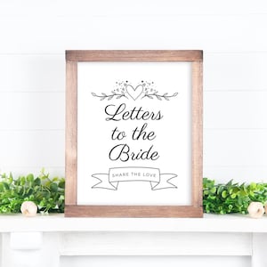 Peut inclure: Un panneau encadré en bois avec l'inscription "Letters to the Bride" en écriture élégante. Le panneau est orné de motifs floraux et de cœurs, avec la phrase "Share the Love" sur une bannière.