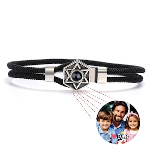 May include: Black braided cord bracelet with a silver charm featuring a six-pointed star with a black stone in the center. The charm has a hidden photo feature that reveals a photo of a father and his two children with the text "I ♥ DAD".