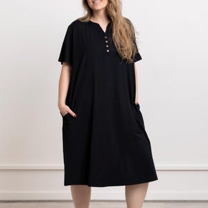 May include: A black knee-length dress with a button-up neckline and short sleeves. The dress has two pockets on the sides.