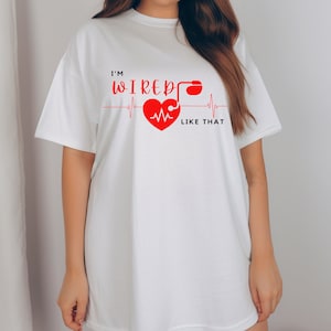 Op de afbeelding: Wit oversized T-shirt met een rode grafische afbeelding met de tekst "I'm wired like that" met een rood hart en een gestileerde EKG-lijn.