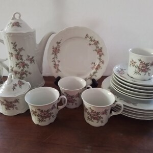 May include: A white porcelain tea set with a floral pattern. The set includes a teapot, creamer, sugar bowl, four cups, and saucers. The floral pattern is in shades of pink and brown.