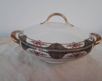May include: White porcelain serving dish with a gold handle and gold trim. The dish has a floral design with pink and green flowers.