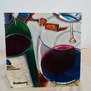 May include: A ceramic tile with a colorful abstract design featuring a wine bottle, a wine glass, and a cork. The tile is signed "Anne Cleary" in the bottom left corner.