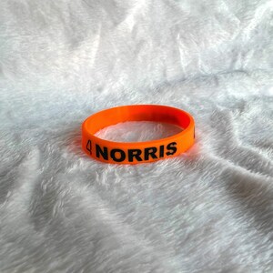 May include: Orange silicone wristband with the text "4 NORRIS" printed in black.