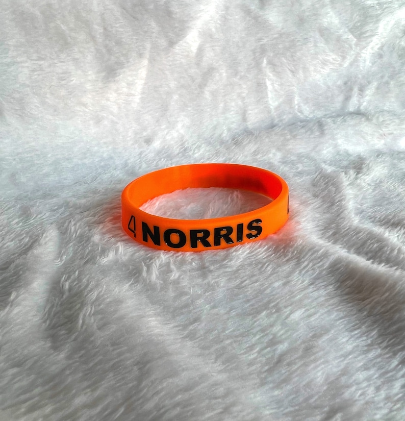 May include: Orange silicone wristband with the text "4 NORRIS" printed in black.