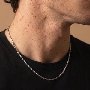Könnte beinhalten: Eine silberne Seilkette. Die Halskette wird um den Hals getragen und liegt auf einem schwarzen T-Shirt. Das Bild ist eine Nahaufnahme von Hals und Gesicht einer Person mit Brille.