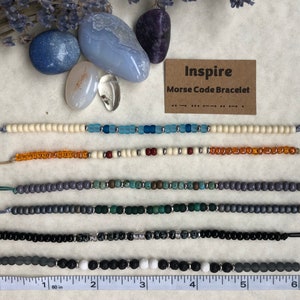 May include: Six beaded bracelets with different colored beads and a ruler for size reference. The bracelets are labeled "Inspire Morse Code Bracelet" with the Morse code for the word "inspire".