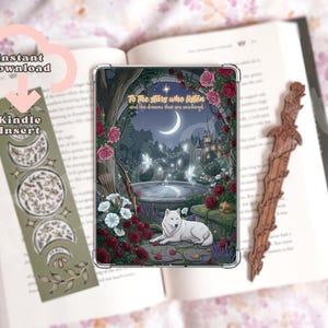 Könnte beinhalten: Ein rechteckiger Kindle-Einsatz mit einer Fantasy-Illustration eines weißen Wolfs, einer Mondsichel, eines Steinbrunnens und roter Rosen. Der Text lautet, To the stars who listen and the dreams that are answered. Ein separates grünes Lesezeichen mit Mondphasen und ein hölzernes Schwert-Lesezeichen sind ebenfalls abgebildet.