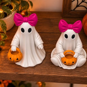 3D printable ghost decoration set with bright pink bows, black oval eyes and jack o lantern candy buckets for Halloween decor.