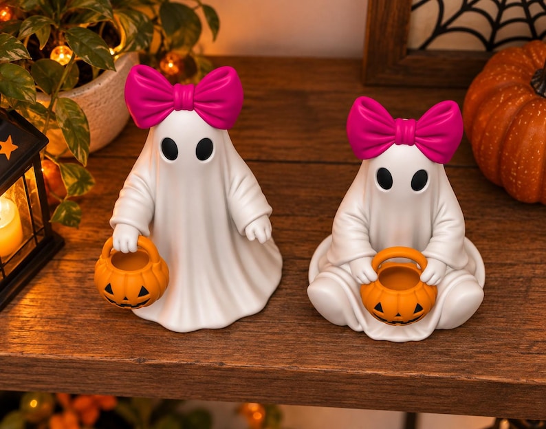 3D printable ghost decoration set with bright pink bows, black oval eyes and jack o lantern candy buckets for Halloween decor.
