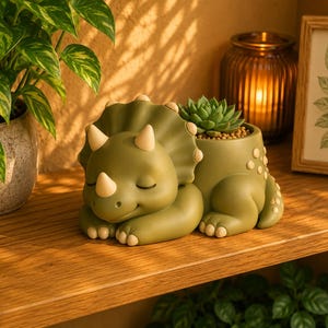 Op de afbeelding: Een groene triceratops plantenpot met een vetplant. De dinosaurus heeft een slapende uitdrukking met gesloten ogen en bruine hoorns. De pot staat op een houten plank.