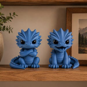 Könnte beinhalten: Zwei blaue Drachenfiguren mit großen Augen und stacheligen Details. Ein Drache hat die Arme verschränkt, der andere hat den Mund offen. Sie werden auf einem Holzregal ausgestellt, was auf ein dekoratives oder sammelbares Thema hindeutet.