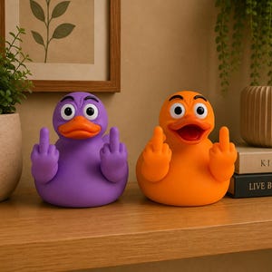 May include: Two rubber ducks, one purple and one orange, each featuring a cartoonish expression with furrowed brows and wide eyes. Both ducks have wings shaped into raised middle fingers, positioned symmetrically on a wooden surface.
