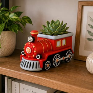 May include: A red and black train-shaped planter with a succulent plant. The planter has a gray front and wheels. The train is sitting on a wooden shelf next to a framed picture and a decorative vase.