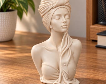 May include: A cream-colored resin bust sculpture depicting a person with closed eyes, wearing a wrapped head towel and a draped towel over the shoulder. The figure has a smooth, matte finish and is sculpted from the chest up with detailed folds.