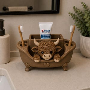 May include: A brown bathtub-shaped toothbrush holder featuring a sculpted Highland cow with horns and fur, holding two bamboo toothbrushes and a tube of Crest Pro-Health Advanced Deep Clean Mint toothpaste in the central compartment.