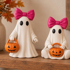 3D printable ghost girl duo for Halloween decor with black oval eyes, pink hair bows and jack o lantern candy baskets displayed in a cozy home setting.