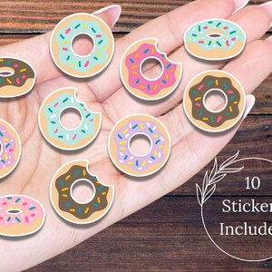 Könnte beinhalten: Zehn Donut-Aufkleber in verschiedenen Farben, darunter Rosa, Blau und Braun, mit Streuseln. Einige Donuts haben einen Biss. Der Text "10 Stickers Included" befindet sich in einem weißen Kreis.
