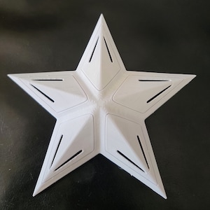 May include: A white, five-pointed star with a textured surface and geometric design. Each point features a series of angled cutouts. The star is likely a decorative item or part of a larger design.