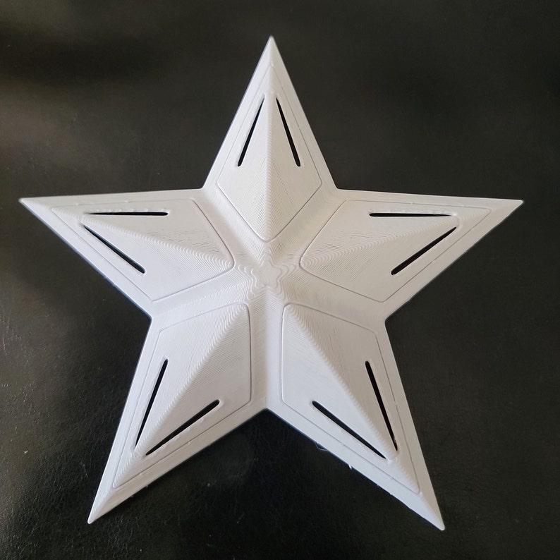 K&ouml;nnte beinhalten: Ein wei&szlig;er, sternf&ouml;rmiger Gegenstand mit f&uuml;nf Spitzen und einer strukturierten Oberfl&auml;che. Es hat ein geometrisches Design mit abgewinkelten Aussparungen an jeder Spitze. Dieses dekorative Objekt k&ouml;nnte f&uuml;r verschiedene Bastel- oder Designprojekte verwendet werden.