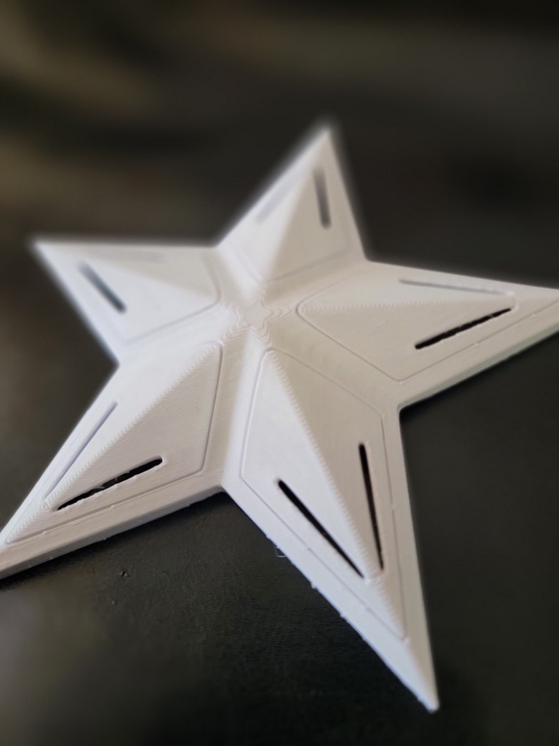 K&ouml;nnte beinhalten: Ein wei&szlig;es, sternf&ouml;rmiges Objekt mit f&uuml;nf Zacken und einem geometrischen Design. Der Stern hat eine strukturierte Oberfl&auml;che und mehrere rechteckige Aussparungen entlang der Kanten jeder Spitze. Das Objekt scheint aus einem festen Material zu bestehen.