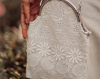 May include: A white crocheted purse with a silver clasp and chain strap. The purse has a floral design with small circles and flowers.