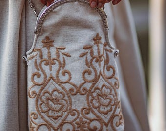 May include: A small, white linen purse with a silver chain strap and a brown embroidered floral design.
