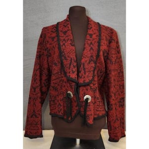 Puede incluir: Chaqueta estampada en rojo y negro con ribete negro y cierres plateados. La chaqueta tiene cuello chal y mangas largas. El estampado es un diseño geométrico. La chaqueta se exhibe en un maniquí.