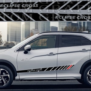 Puede incluir: Un Mitsubishi Eclipse Cross plateado con rayas de carreras negras y rojas a los lados. El coche tiene ruedas negras y las palabras "ECLIPSE CROSS" están impresas en el lateral del coche.