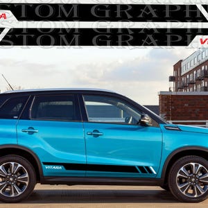 Può includere: Una Suzuki Vitara blu con strisce laterali nere e la scritta "Vitara" sul lato. L'auto è parcheggiata su una strada con un edificio in mattoni sullo sfondo.