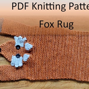 Könnte beinhalten: Ein gestrickter Fuchs-Teppich in Orange, Weiß und Grau. Der Teppich ist in Form eines liegenden Fuchses mit Kopf, Ohren, Schwanz und Pfoten. Der Teppich hat schwarze Knopfaugen.