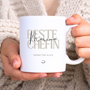 May include: White ceramic mug with the text "Beste Marina Chefin" in brown and black lettering. The text "Danke fur alles" is printed below the main text. A smiley face is printed below the text.
