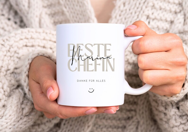 May include: White ceramic mug with the text "Beste Marina Chefin" in brown and black lettering. The text "Danke fur alles" is printed below the main text. A smiley face is printed below the text.