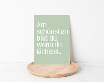 May include: A light green card with white text that reads "Am schönsten bist du, wenn du lächelst."  The text is in a simple, modern font. A small smiley face is at the bottom of the card.